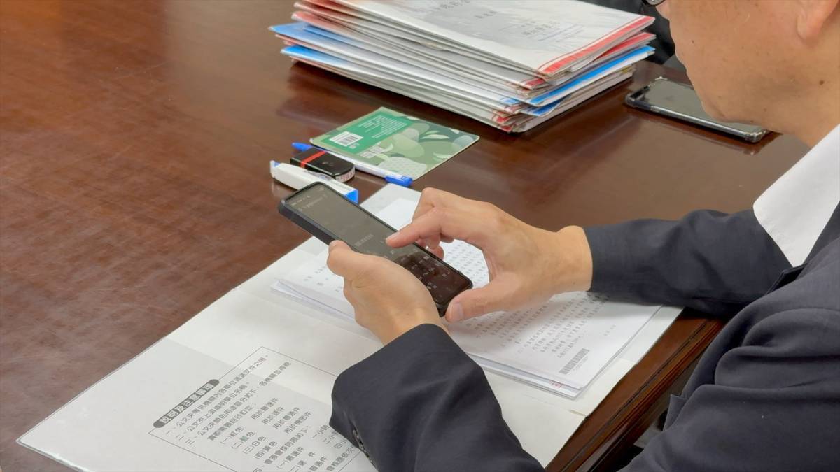 張善政拿著「自製」的小墊板批公文，因為公文附件多，簽名時難免凹凸不平。而他批公文有三寶 : 圖章、立可帶和小墊板，近來也有AI加入討論。